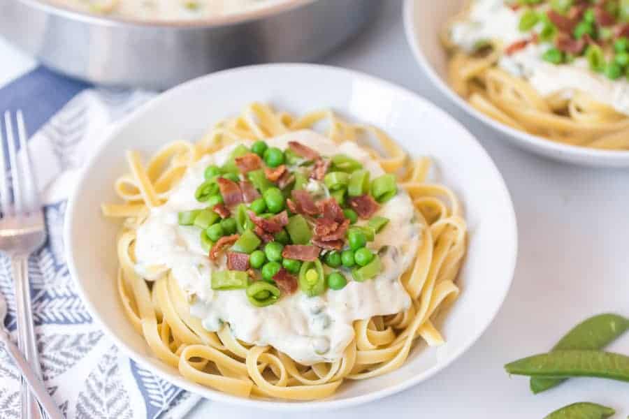 round white bowl of bacon and pea pasta with fork and sugar snap peas