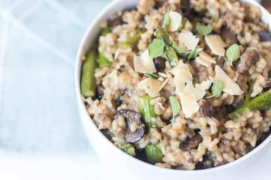 close up - mushroom and asparagus risotto in a bowl garnished with cheese shavings