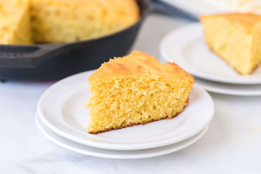 one slice of cut cornbread on a white plate ready to eat