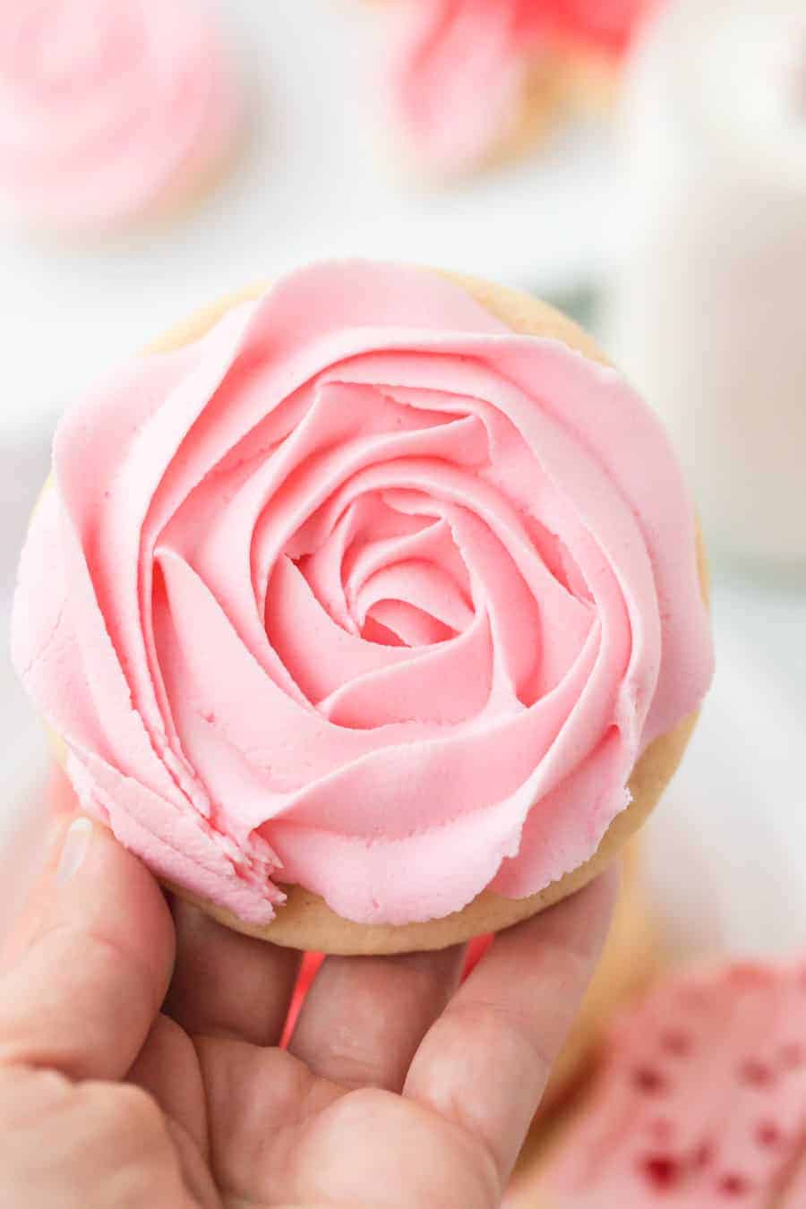 woman holding iced sugar cookie cutout with pink rose icing