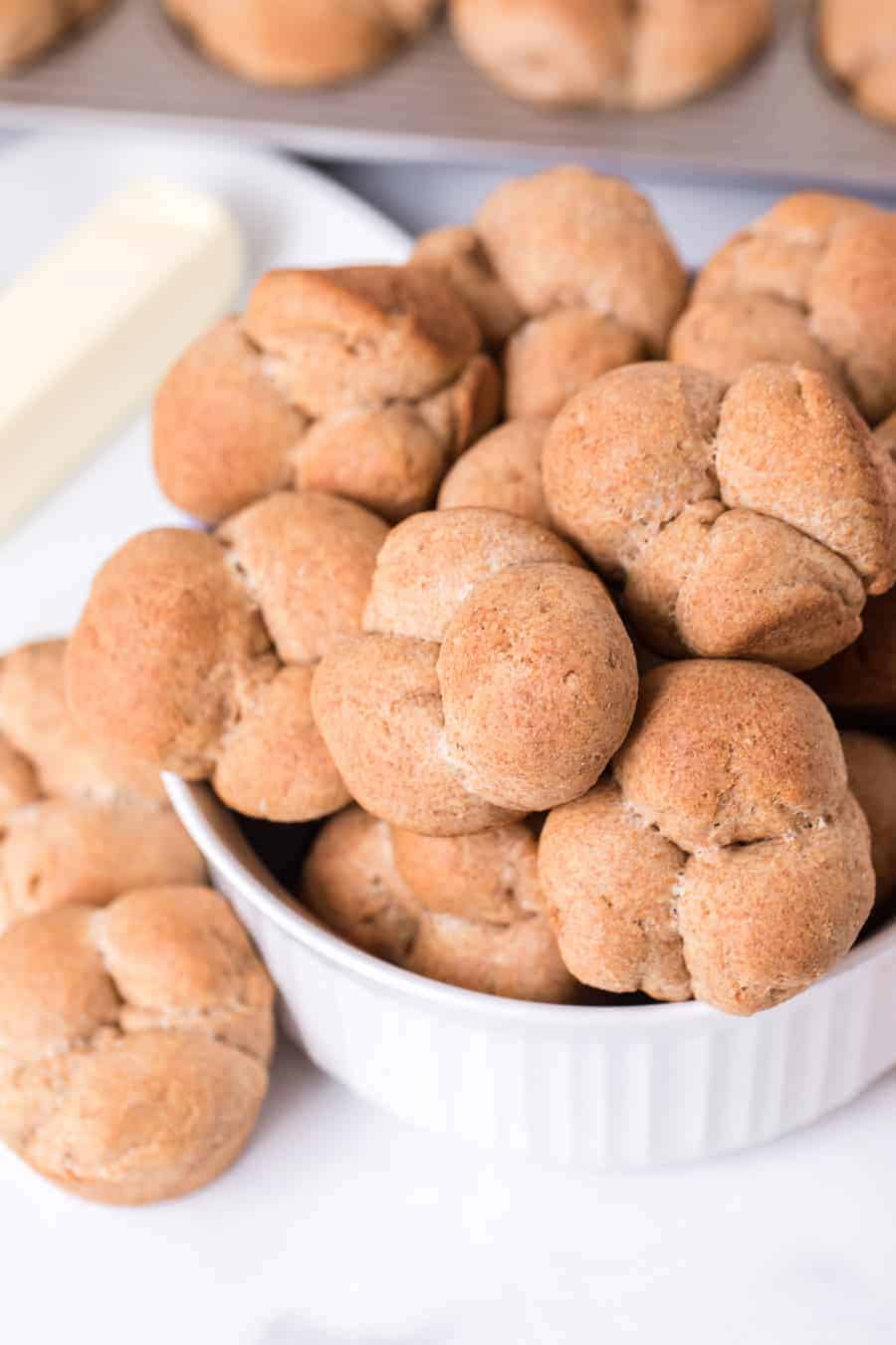 whole wheat clover rolls in white dish next to stick of butter on white surface