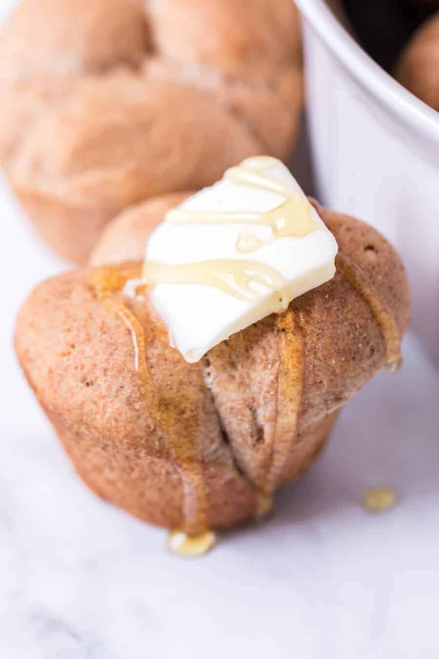 whole wheat clover rolls with pat of butter and drizzled with honey on white surface