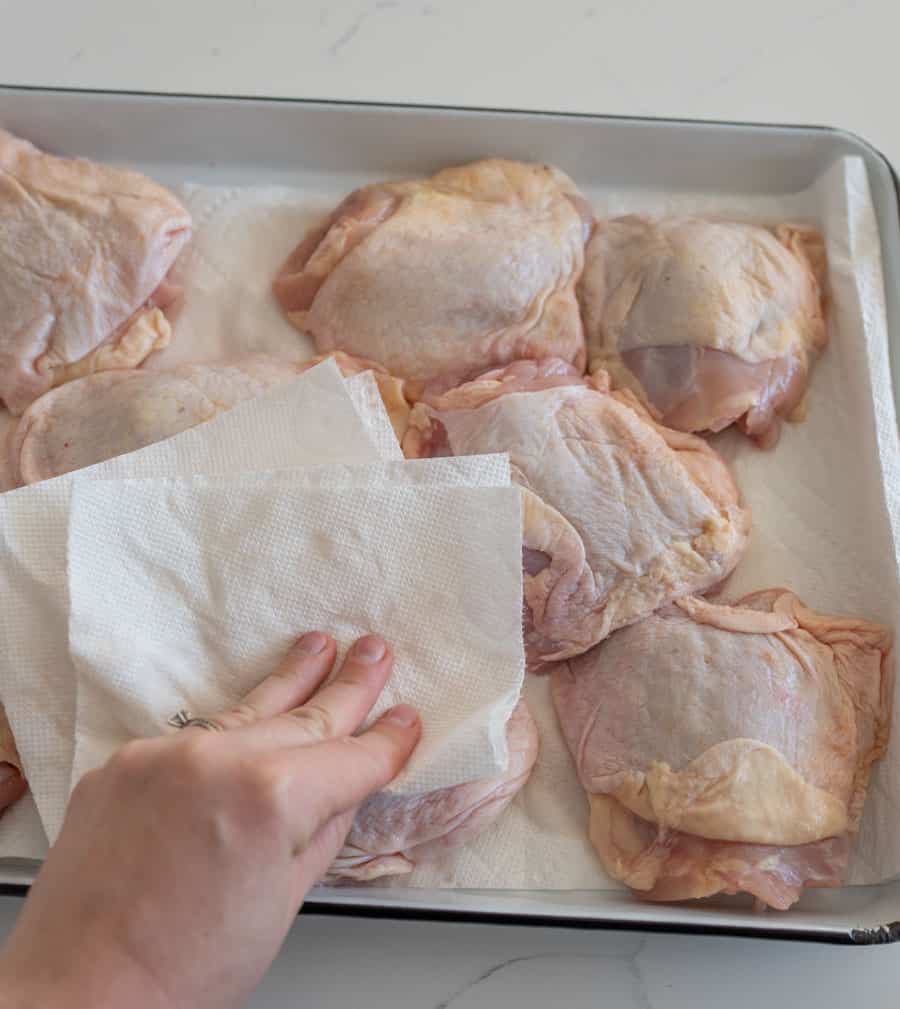 a hand tamping excess water or liquid from the chicken thighs.