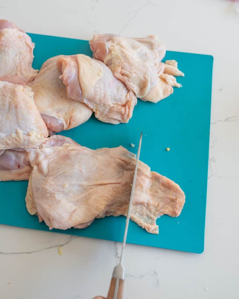 cutting and trimming raw chicken thighs.
