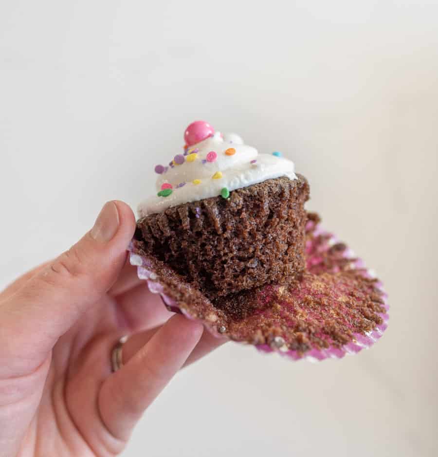 woman holding chocolate cupcake with vanilla frosting with wrapper pulled off 