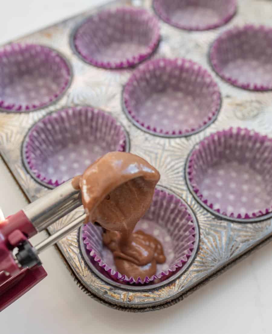 spooning chocolate cake mix into cupcake wrappers in muffin tin