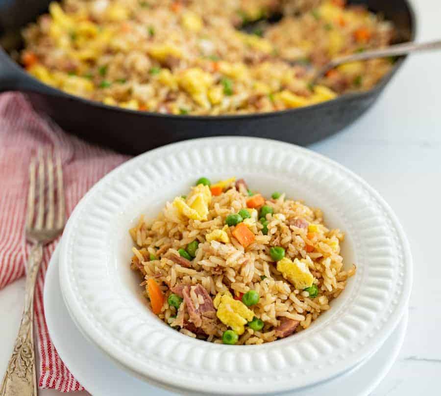 white bowl of fried rice with ham next to fork and skillet of easy fried rice