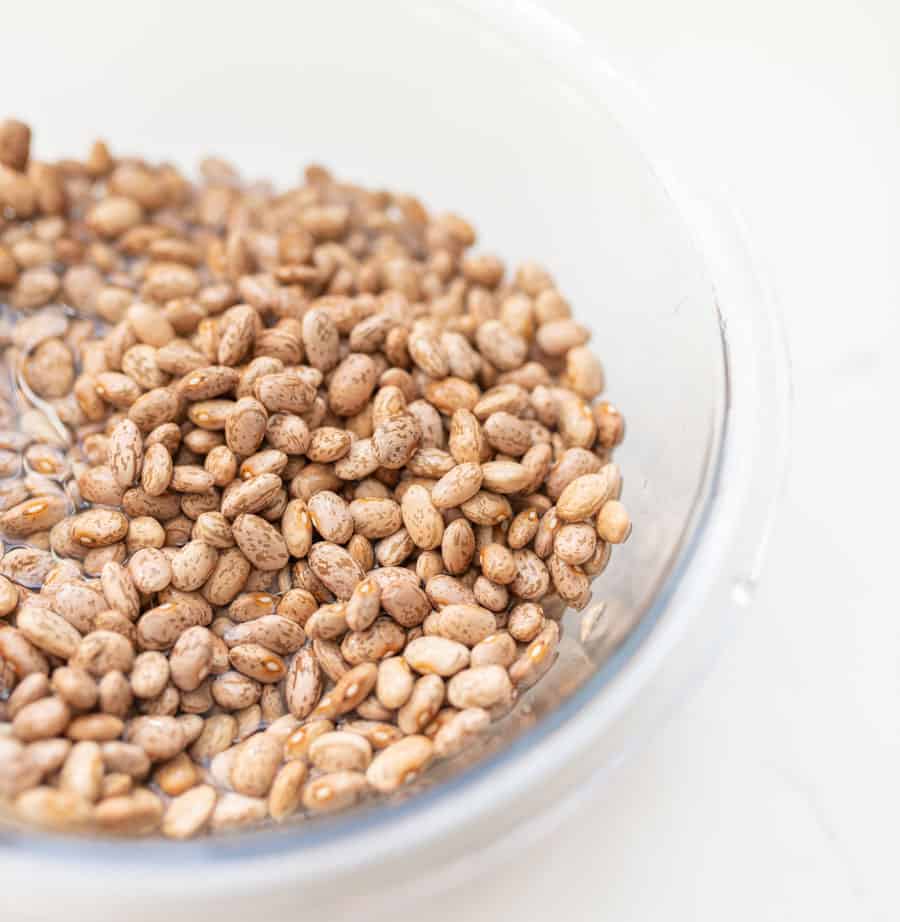 clear glass bowl of uncooked pinto beans soaking in water