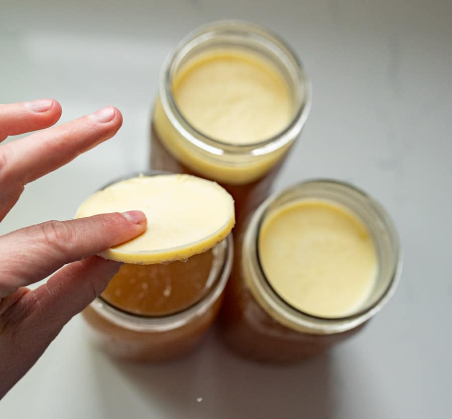 woman holding the fat from the bone broth over three canning jars