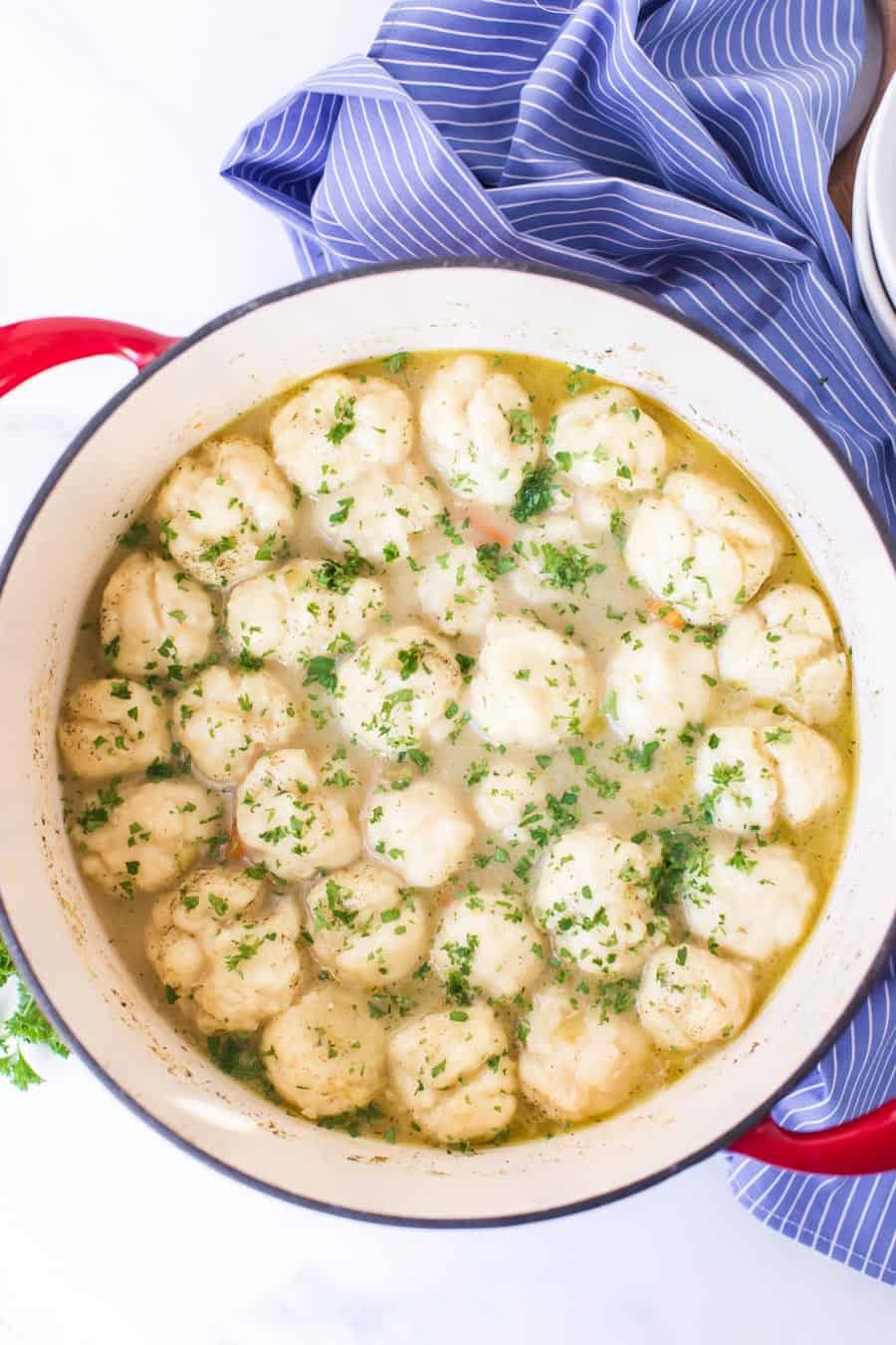 dumplings and soup in a dutch oven on blue and white striped towel