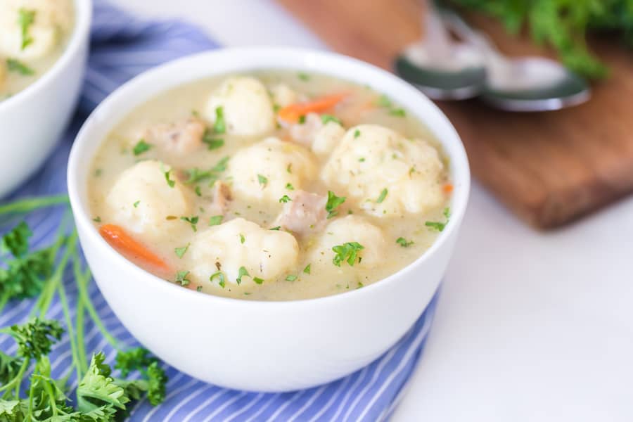 white bowl filled with old fashioned chicken and dumplings on blue and white striped towel with garnish