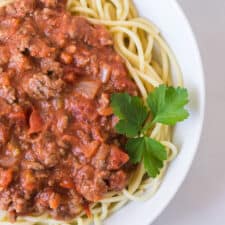 round white bowl of homemade bolognese sauce with garnish on white tablecloth