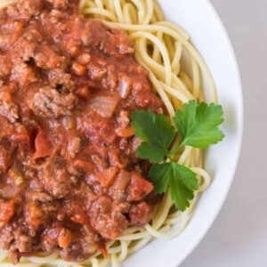 round white bowl of homemade bolognese sauce with garnish on white tablecloth