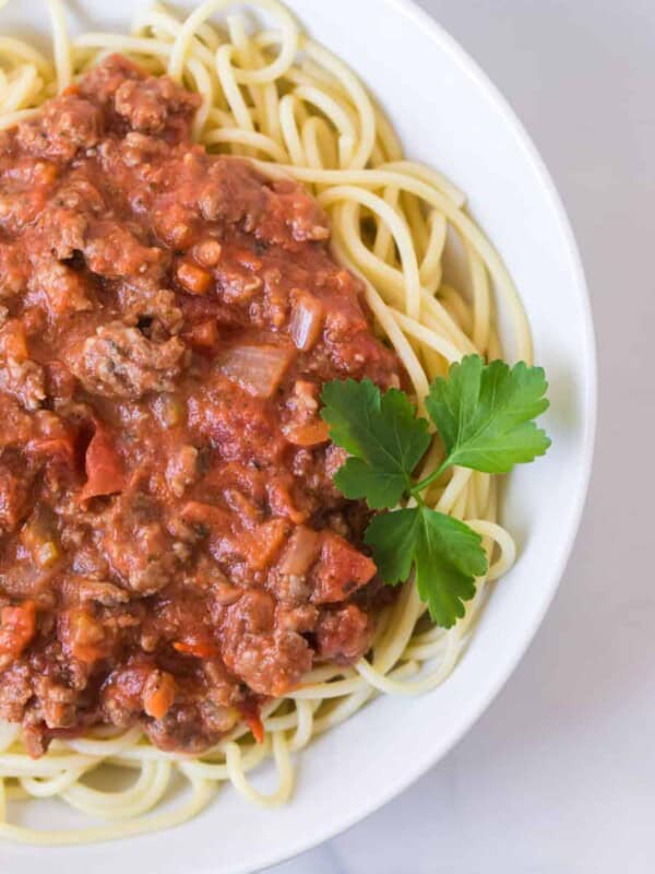 round white bowl of homemade bolognese sauce with garnish on white tablecloth