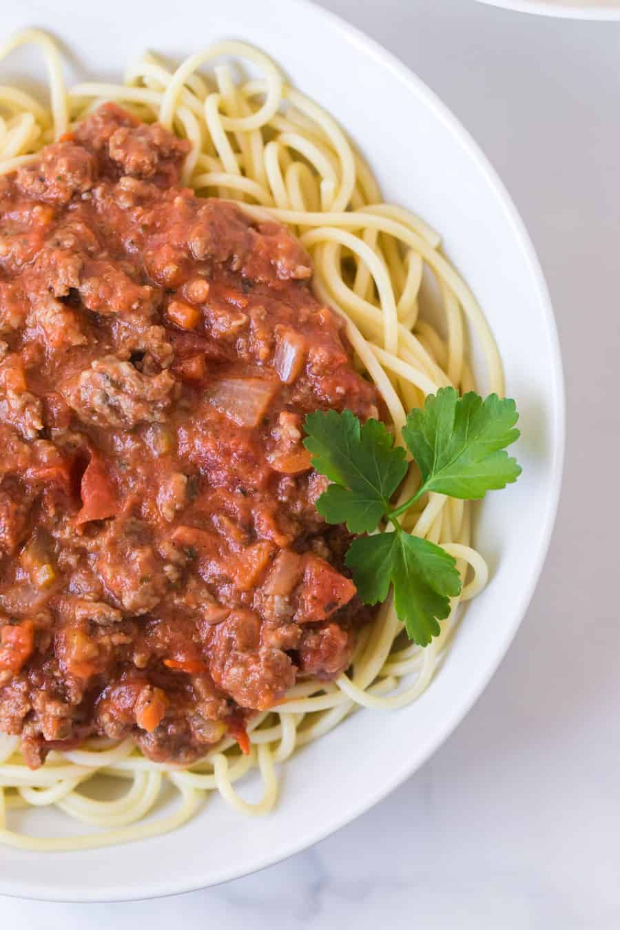 round white bowl of spaghetti with homemade bolognese sauce and garnish