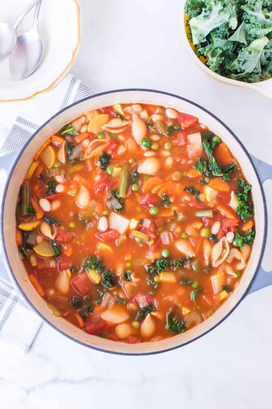 bowl of minestrone soup with cup of kale next to spoons