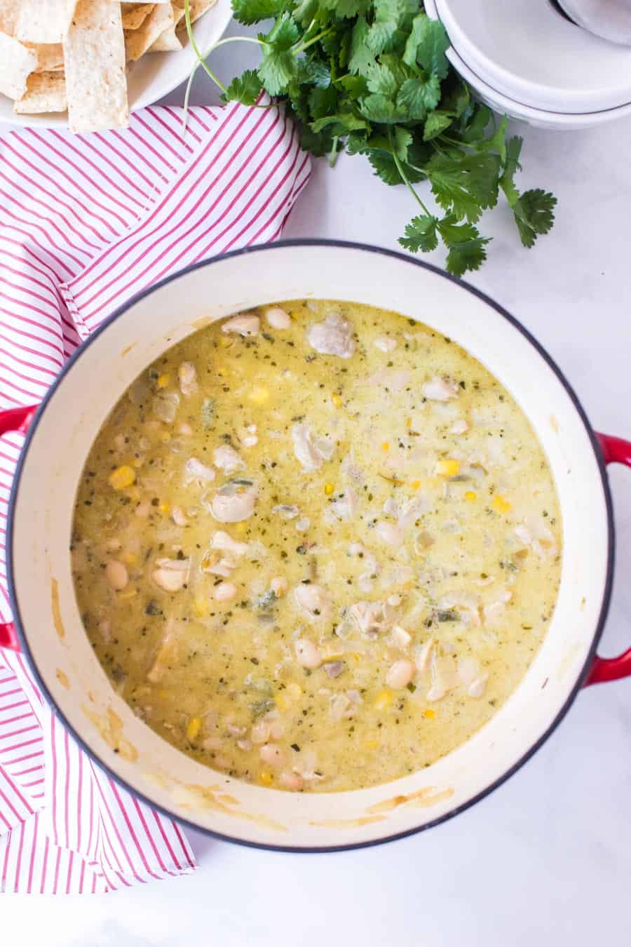 white dutch oven pot with red handles filled with white bean chicken chili on white and red striped towel