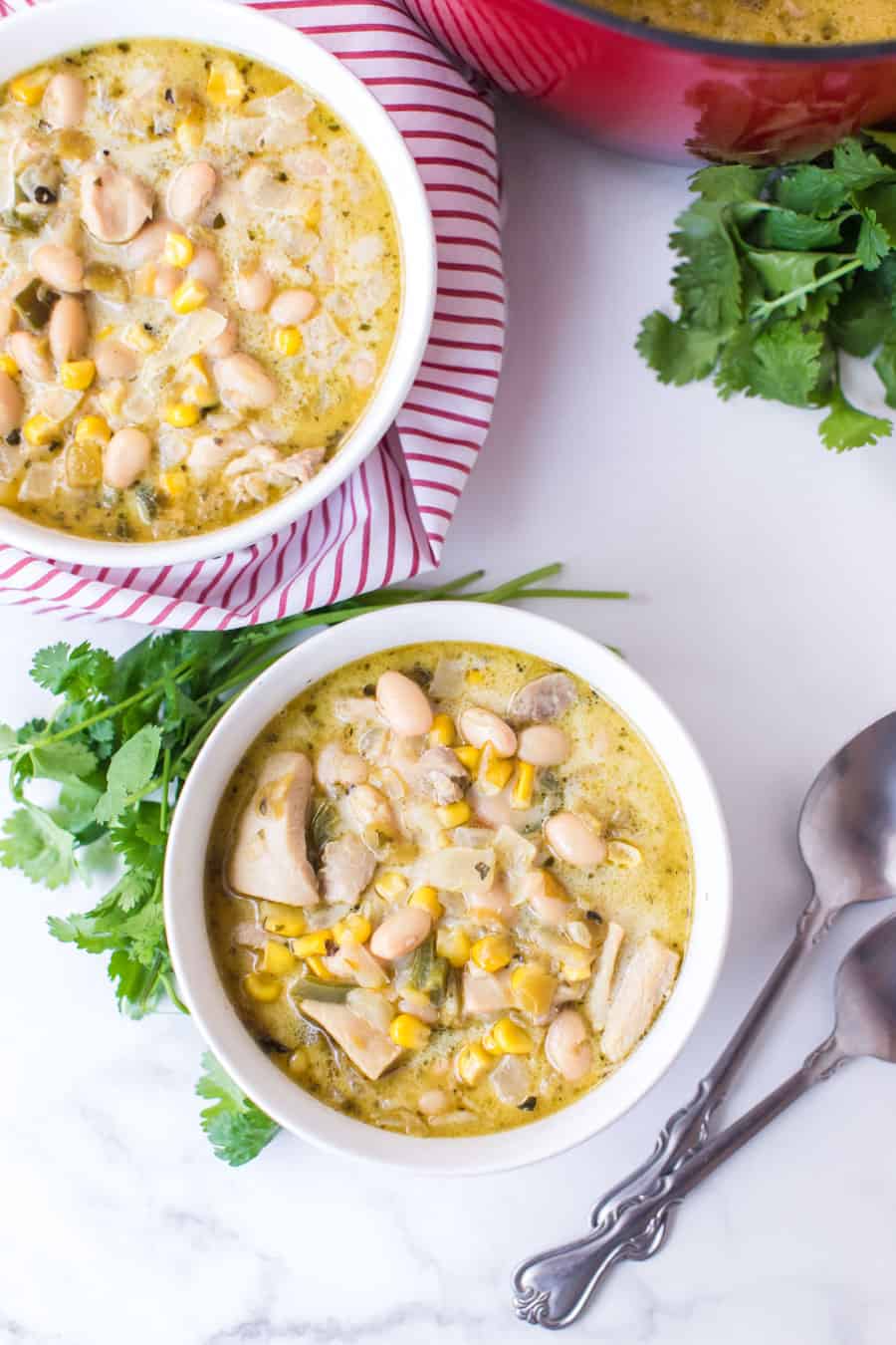 two white bowlfuls of chicken and white bean chili with two spoons and garnish