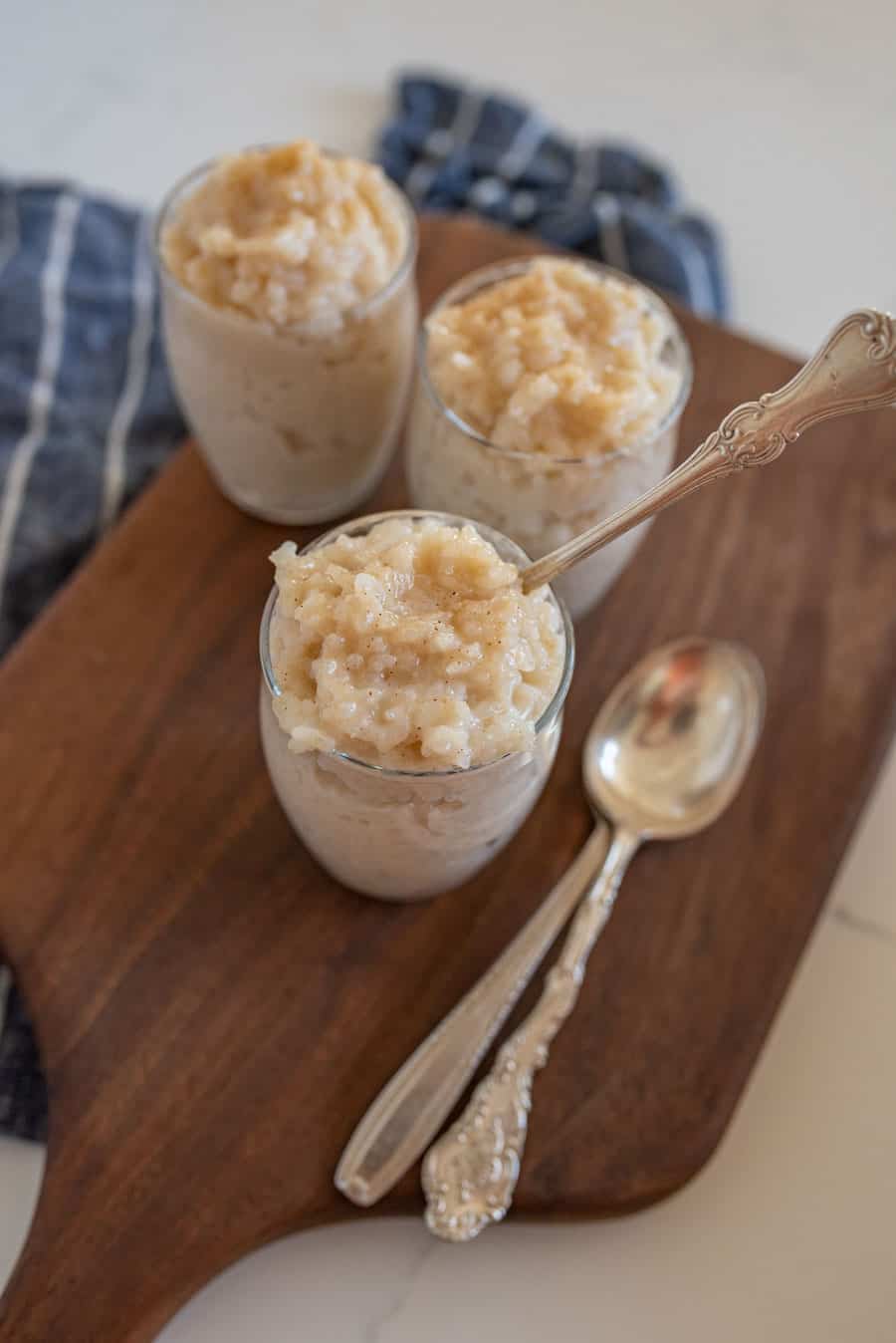 three individual servings of instant pot rice pudding with spoons on wooden cutting board