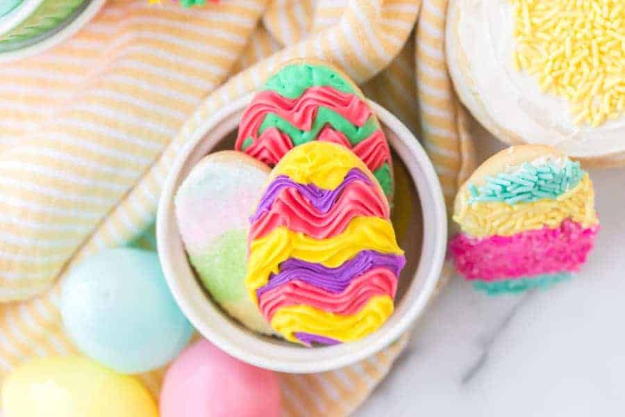 frosted easter sugar cookies in white ramekin and plastic easter eggs on yellow and white striped towel