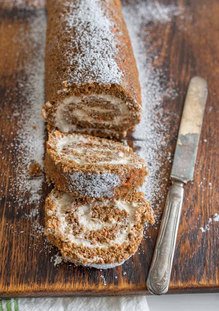 closeup of carrot cake roll on wooden cutting board with butter knife