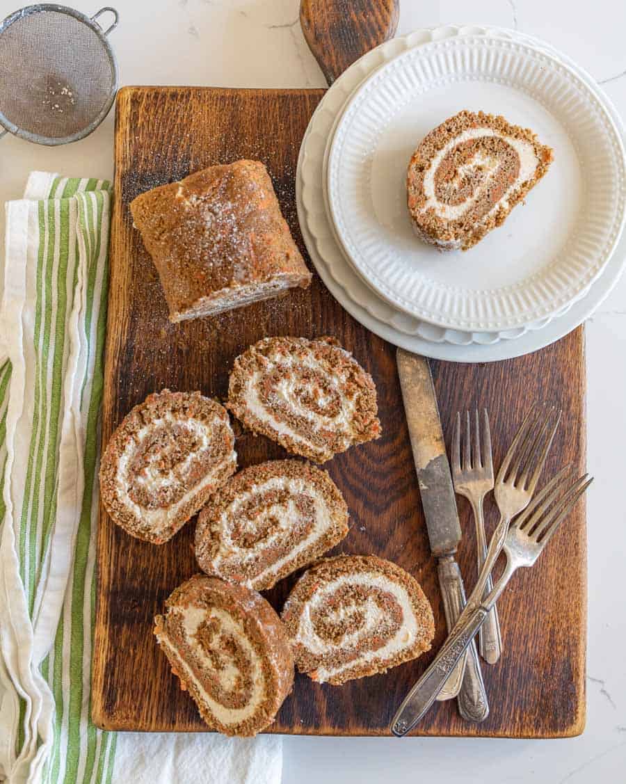 overhead shot of carrot cake roll slices on cutting board with utensils and round dessert plates