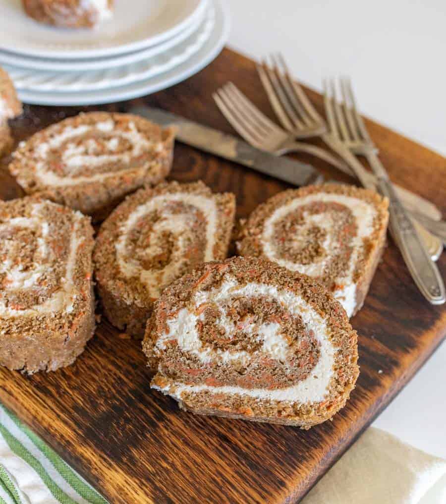 slices of carrot cake roll on wooden cutting board with forks and round white dessert plates