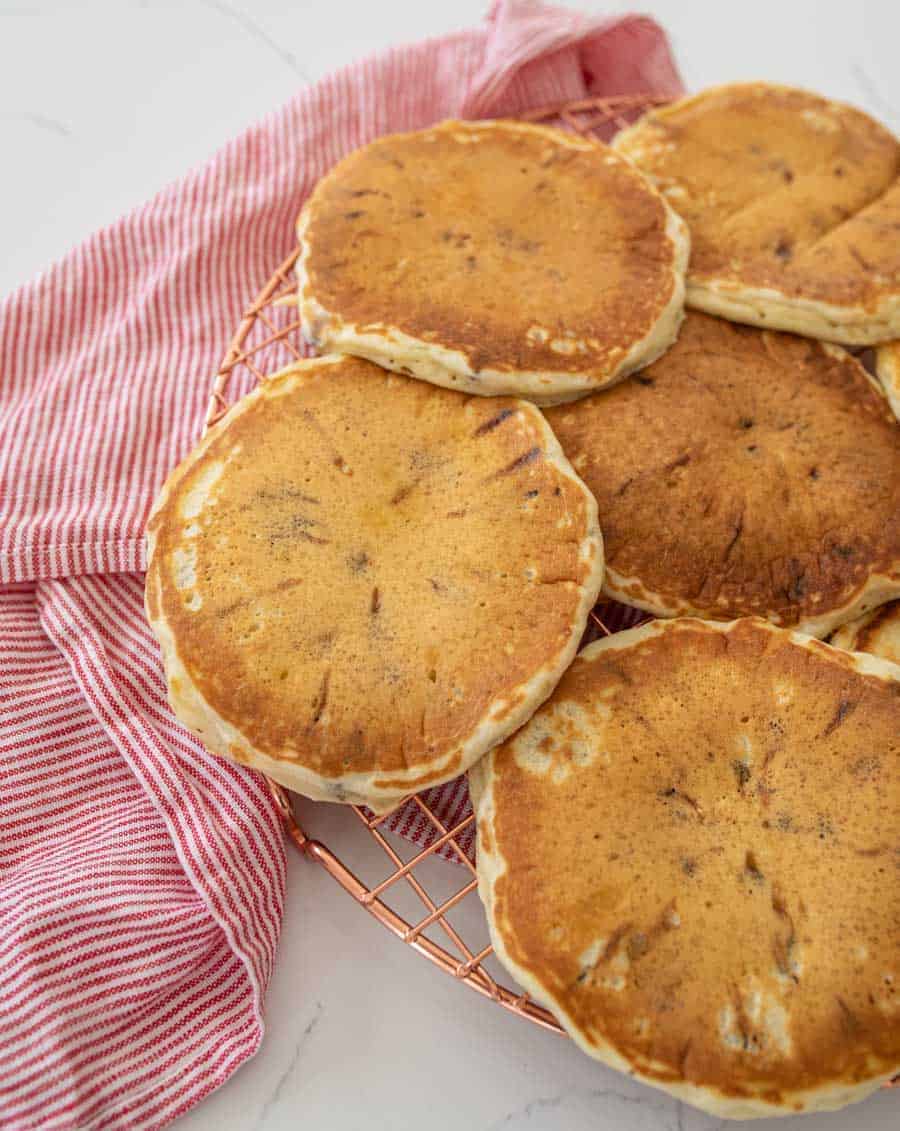 closeup fluffy chocolate chip pancakes on cooling rack on white countertop with red and white striped kitchen towel