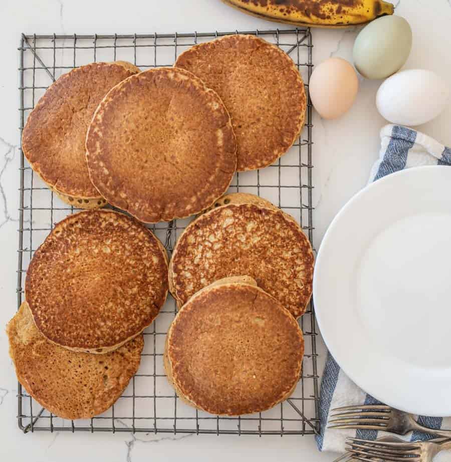 healthy banana pancakes on cooling rack next to round white plate multicolor eggs forks