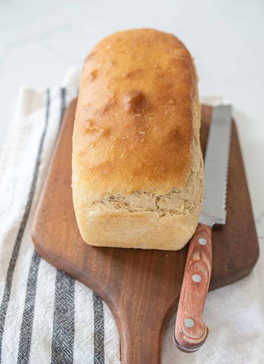 soft sandwich sourdough bread loaf uncut on wooden cutting board with knife