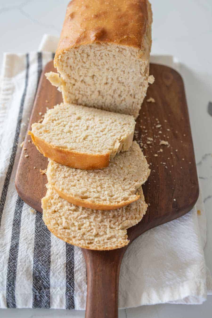 slices of soft sandwich loaf sourdough bread on wooden cutting board with white and blue striped towel underneath