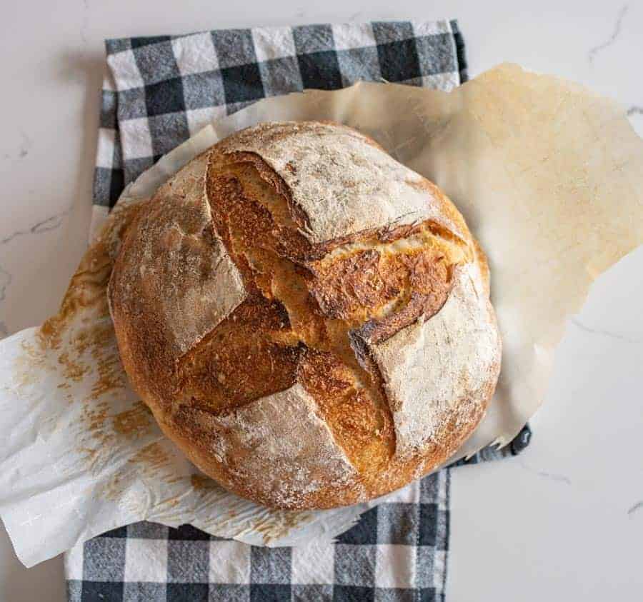 loaf of sourdough bread on parchment and black and white towel