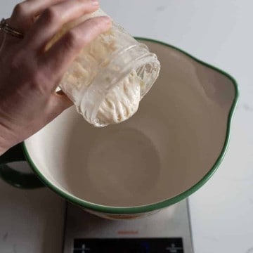 woman pouring sourdough starter in measuring cup