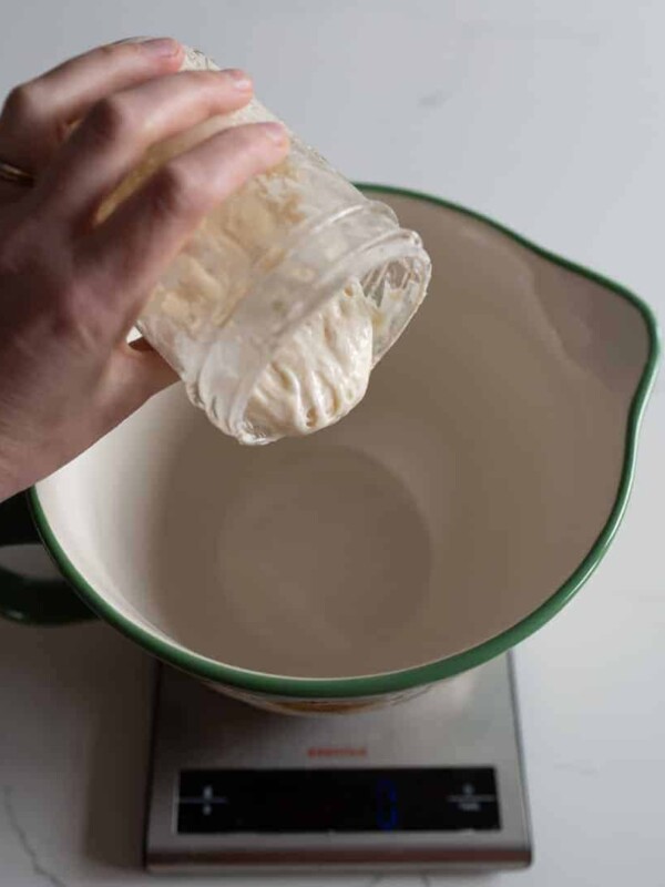 woman pouring sourdough starter in measuring cup