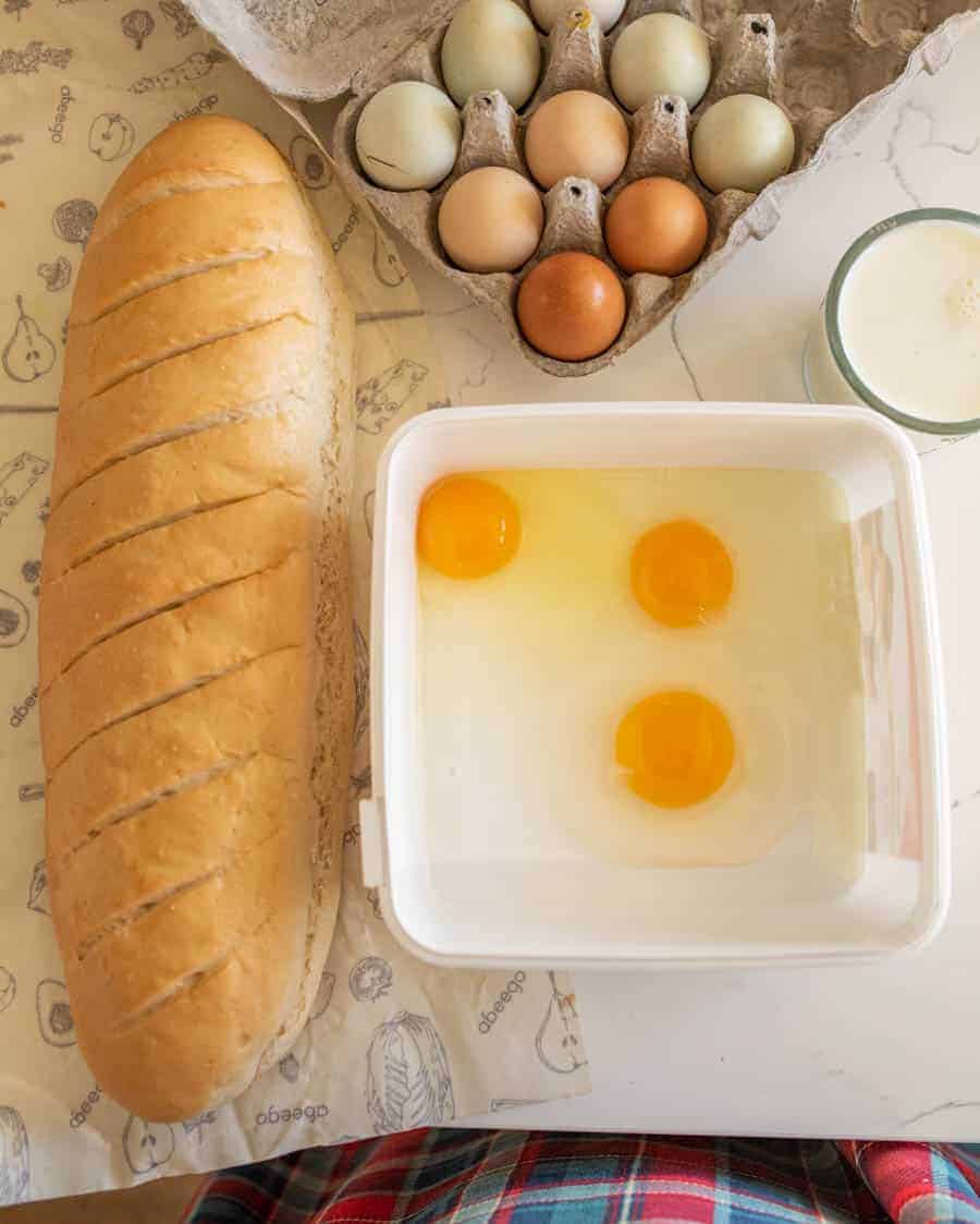 loaf of bread on counter next to bowl of eggs and carton of eggs