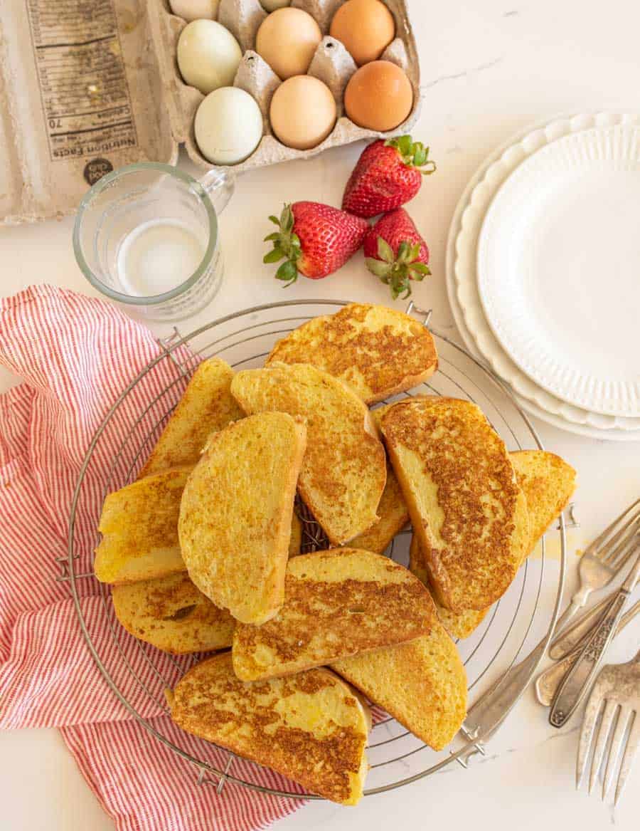 french toast on cooling rack next to forks and carton of eggs and strawberries