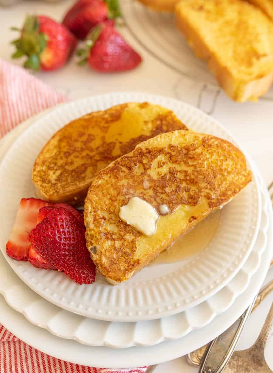 closeup image of two slices of french toast with butter and strawberries on round white plates