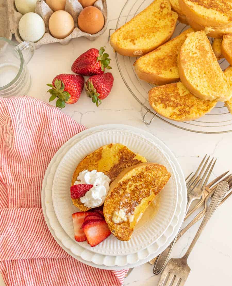 french toast on round white plate with butter and strawberries with forks next to carton of eggs