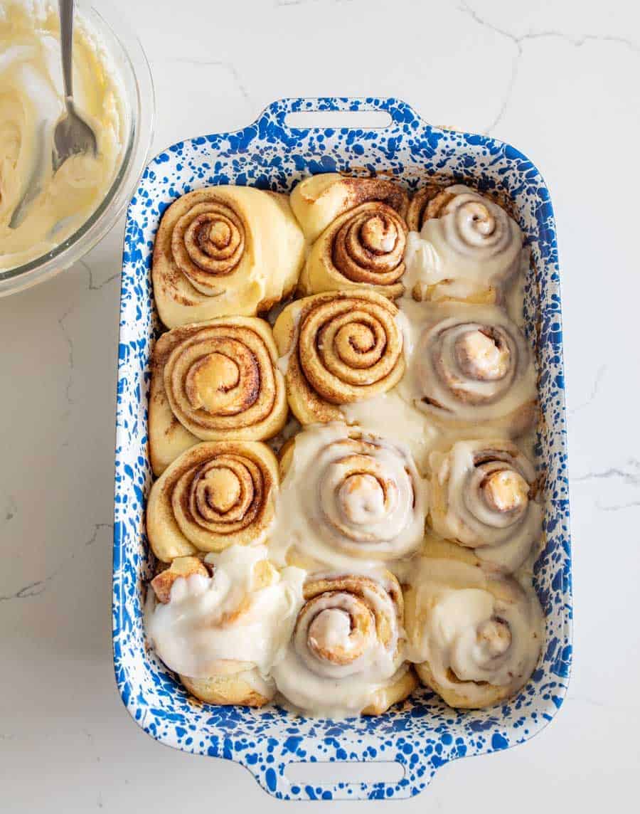 baked sourdough cinnamon rolls in blue and white pan half with buttercream frosting