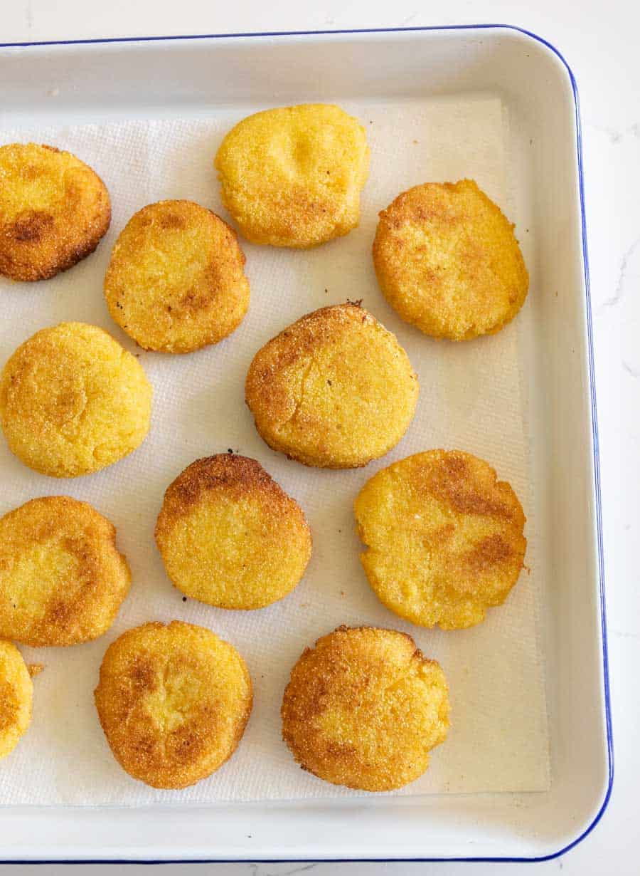 hot water cornbread resting on paper towel on white baking sheet.