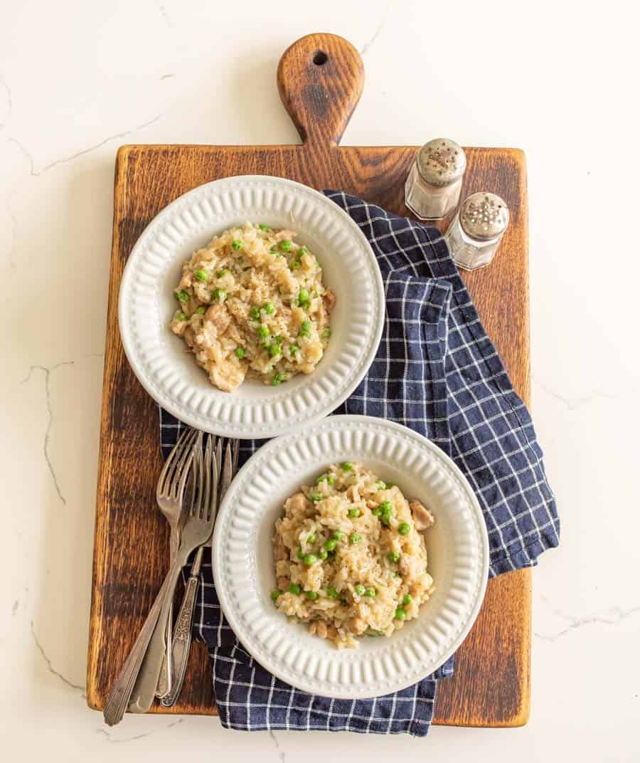 two bowls of chicken and rice on cutting board with forks and salt and pepper