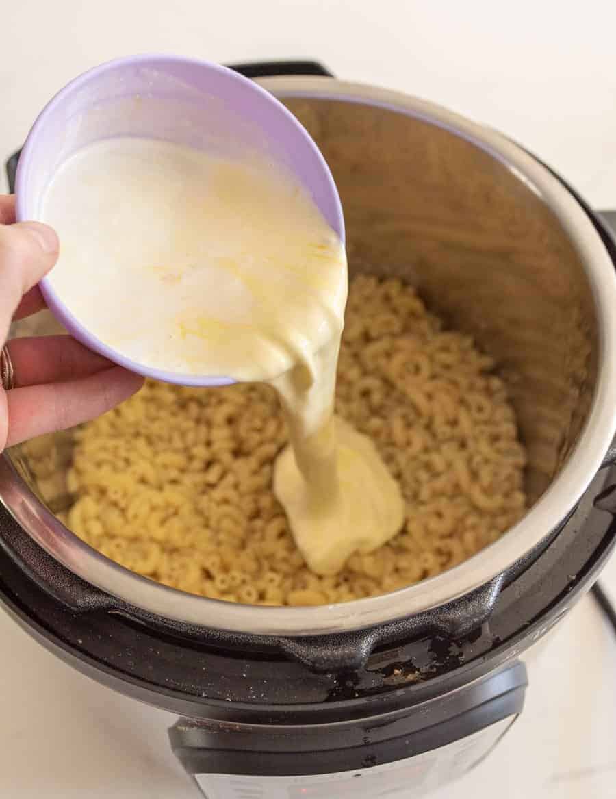 cream and egg being poured into instant pot on top of cooked macaroni