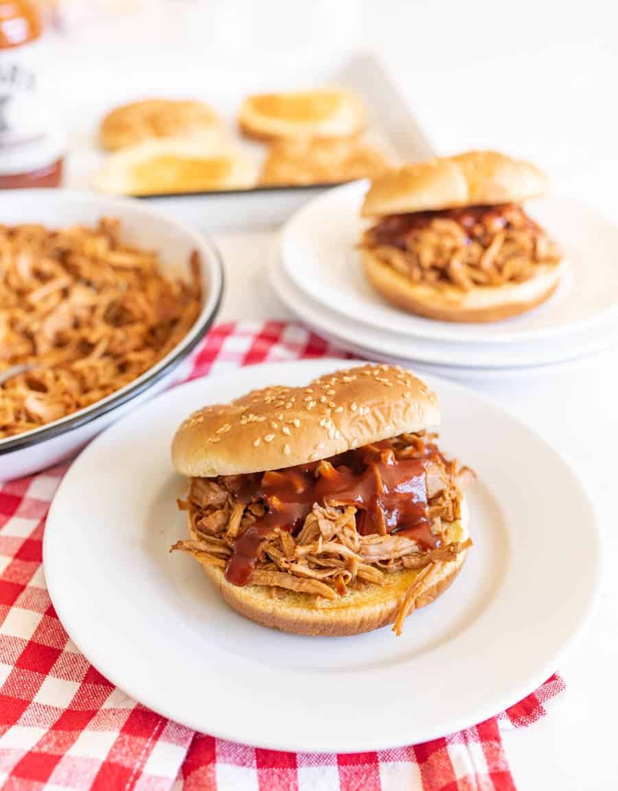 pulled pork sandwich on white plate on bun with extra barbecue sauce