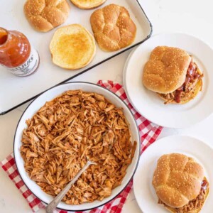 table setting of pulled pork, sandwiches on plates, toasted bun on pan