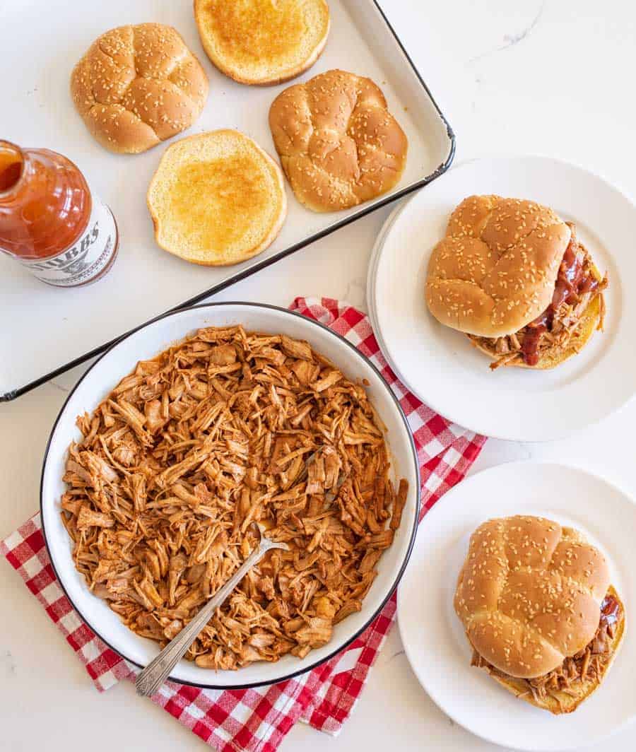 table setting of pulled pork, sandwiches on plates, toasted bun on pan