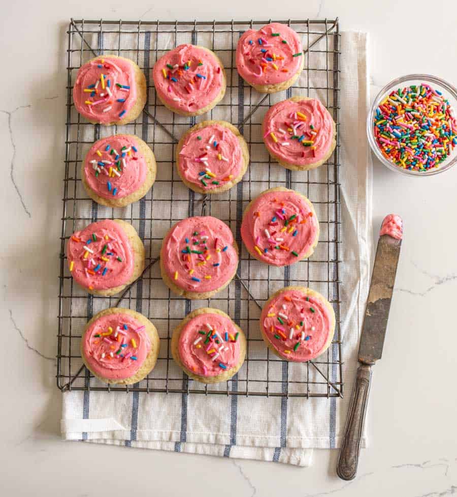 pink frosted cookies with sprinkles on cooling rack next to bowl of sprinkles