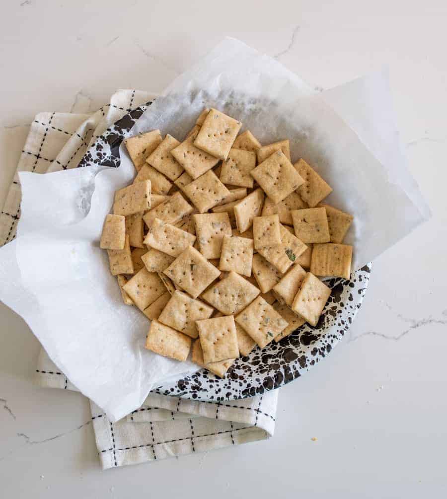 herb and garlic sourdough crackers on parchment in black and white bowl on white countertop