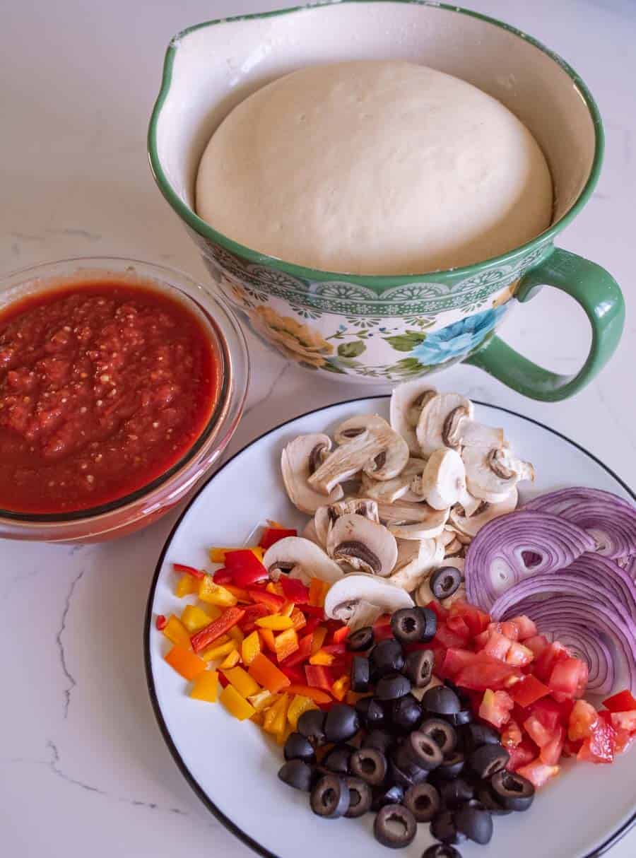 plate of olives tomato red onion bell pepper and mushrooms with pizza sauce and dough rising