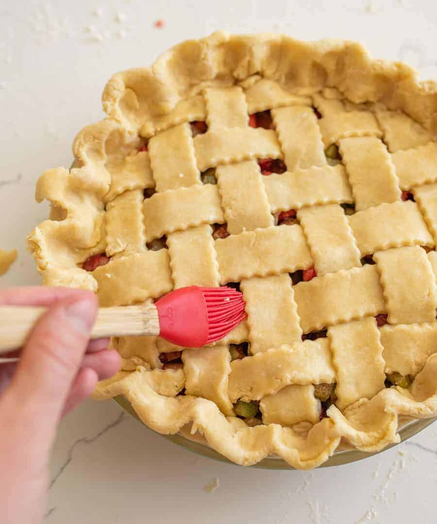 red pastry brush adding water to top of latticed pie crust