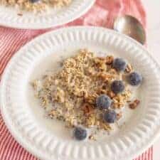 two white bowls of steel cut oats with fruit on red and white striped towel